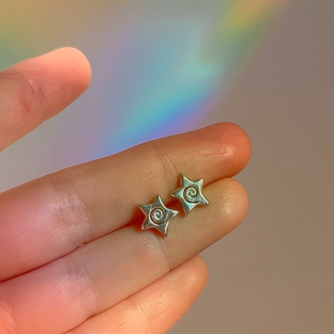 Star-shaped earrings held between fingers with a rainbow background
